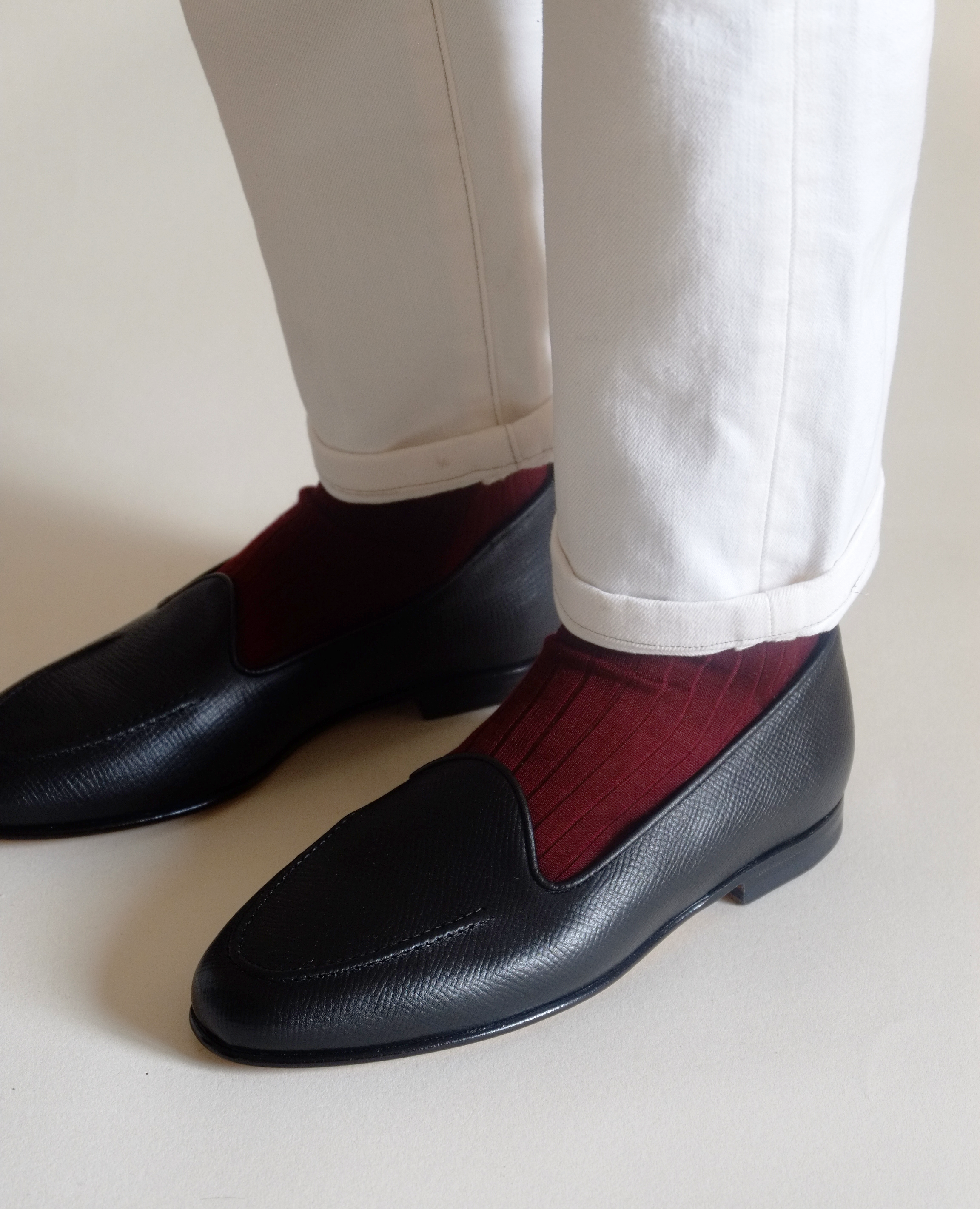 Black loafers with red accents worn with white pants on a light background